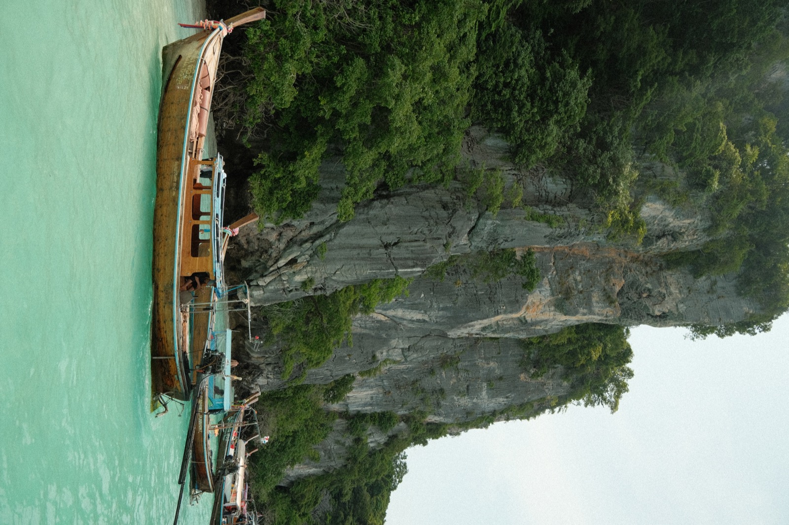 Wooden boats beneath a forested limestone cliff at Phi Phi Island, Thailand