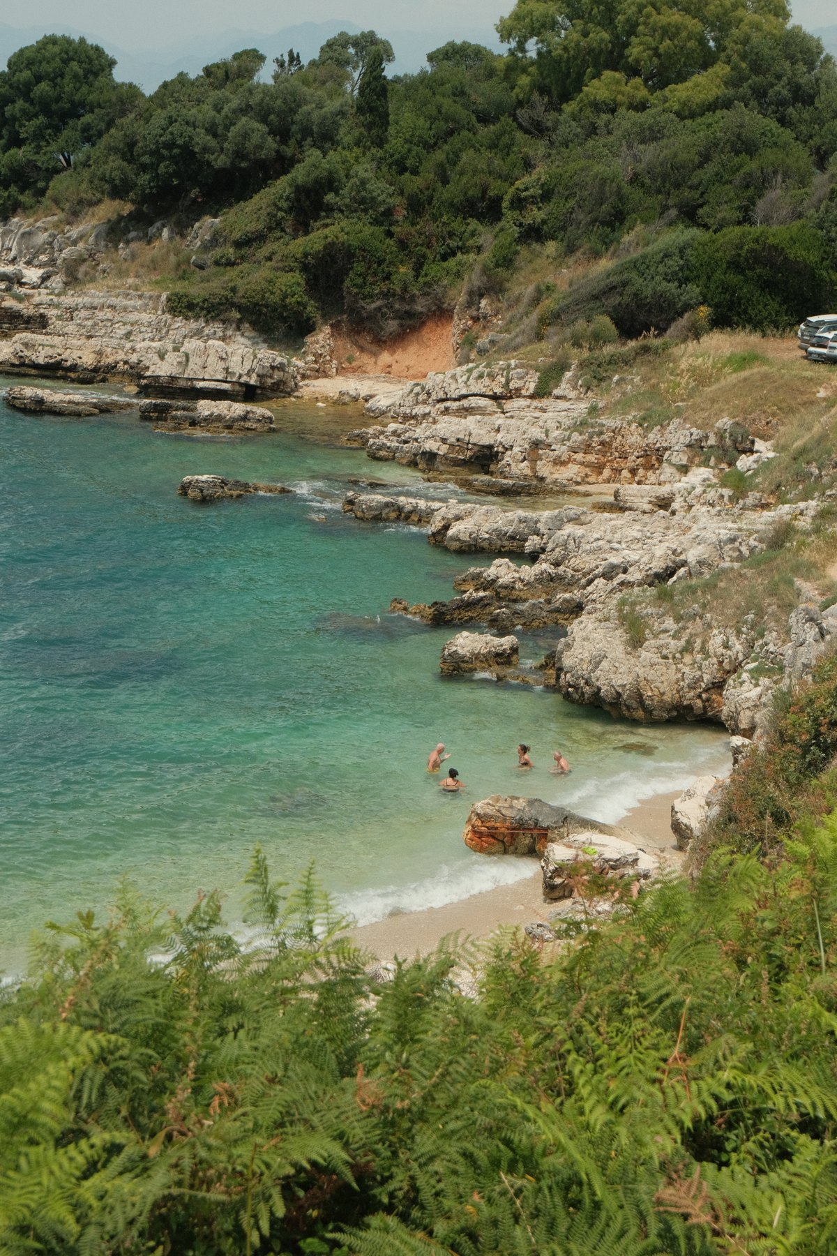 Swimmers in a turquoise cove bordered by rocks and green hills in Corfu, Greece