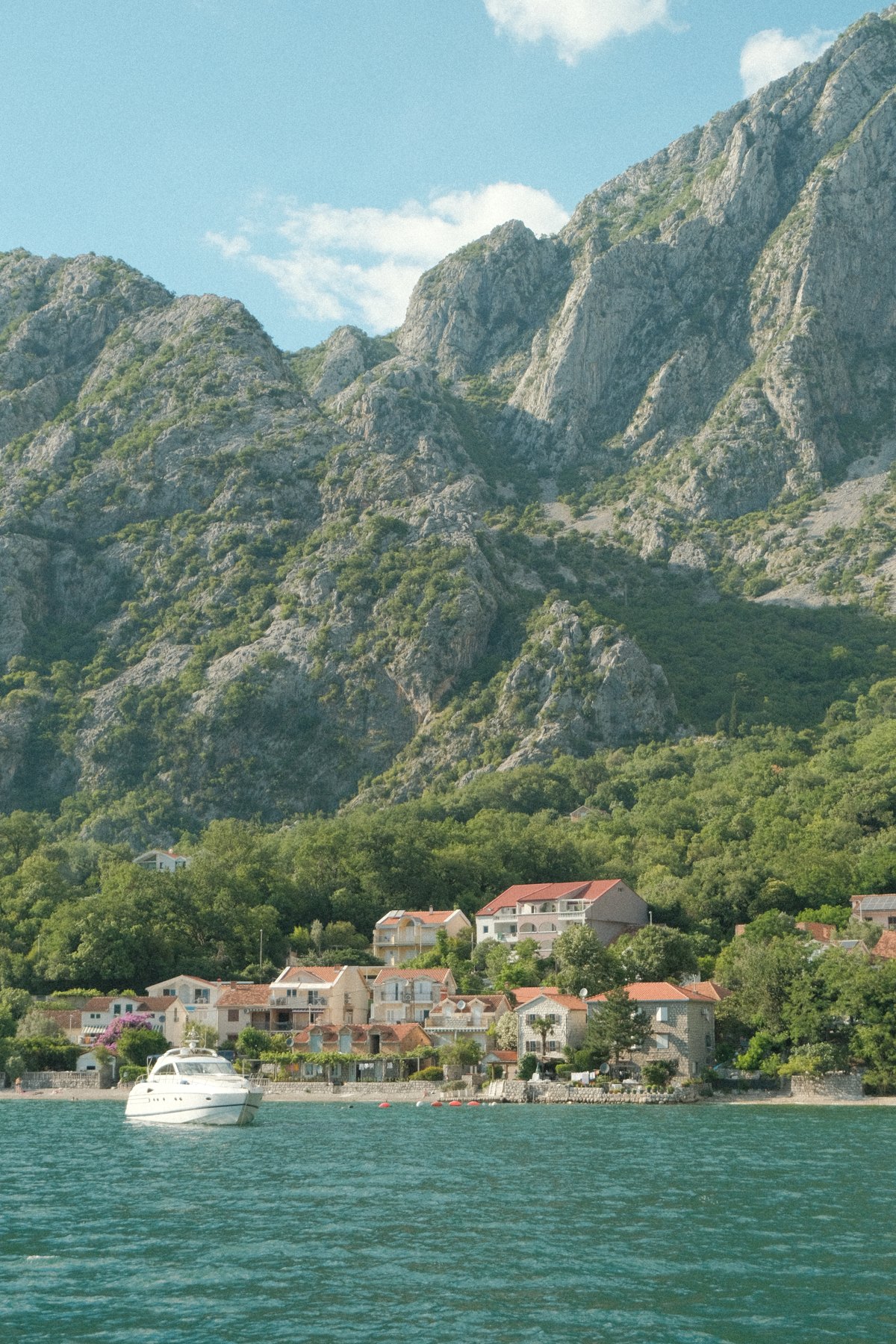 Waterfront homes beneath rugged green mountains in Kotor, Montenegro
