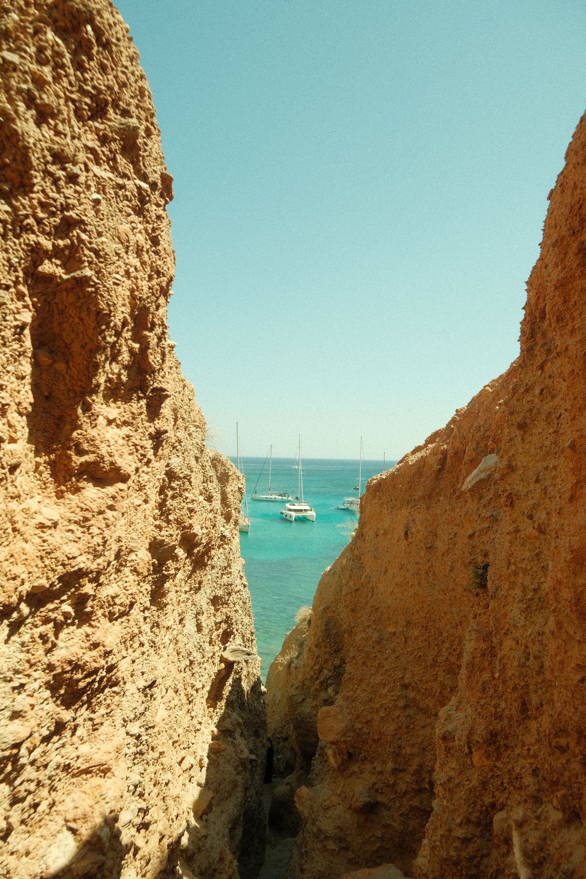 Sailing boats on turquoise water framed by golden cliffs in Milos, Greece